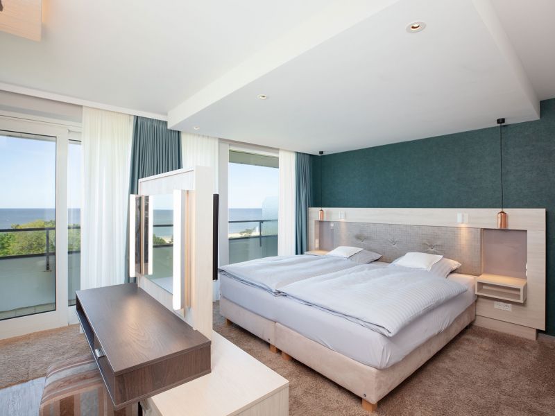 Modern two-room suite with two single beds, a large window with sheer curtains, a balcony, a desk with mirror and a view of the North Sea.