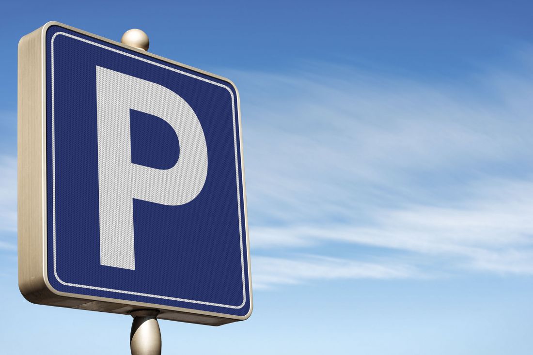 A blue parking sign with a large white P on it stands against a clear blue sky with wispy clouds.